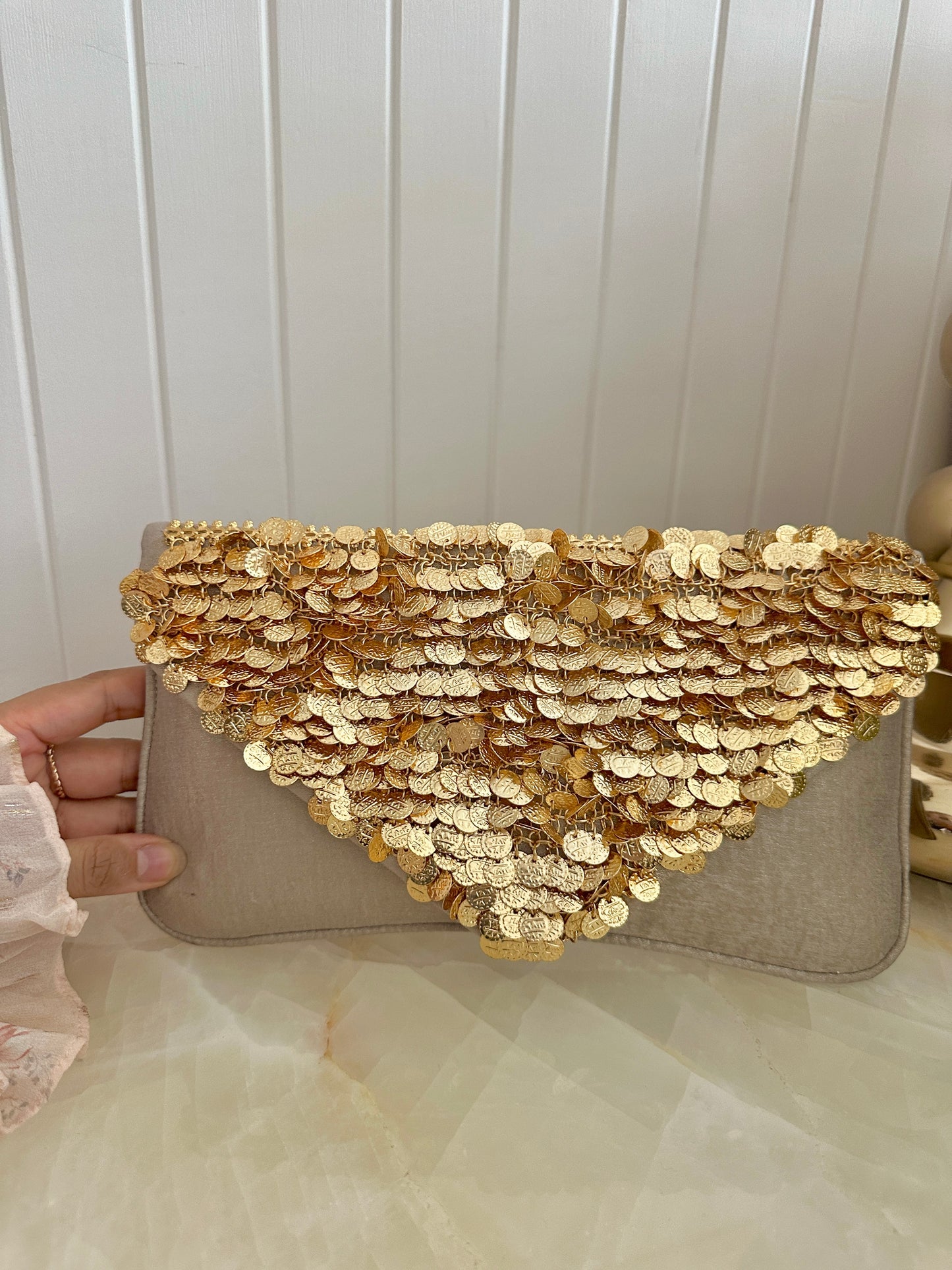 Clutch bag with gold sequin embellishments held by a hand against a white background